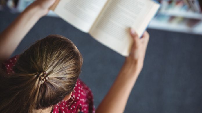 High angle view of attentive schoolgirl reading book in library at school